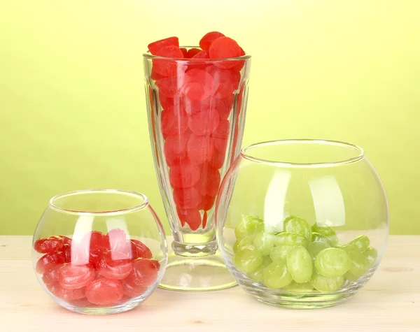Farbbonbons in Gläsern auf Holztisch auf grünem Hintergrund — Stockfoto