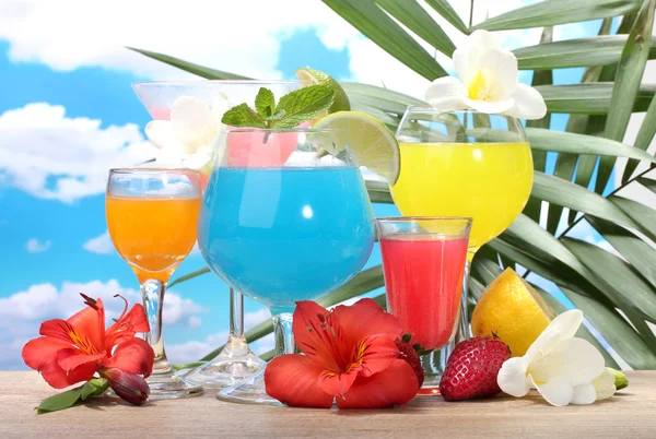 Exotic cocktails and flowers on table on blue sky background — Stock Photo, Image