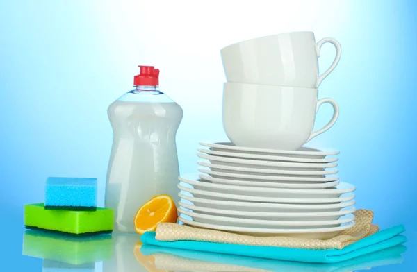 Lege schoon borden en kopjes met afwasmiddel, sponsen en citroen op blauwe achtergrond — Stockfoto