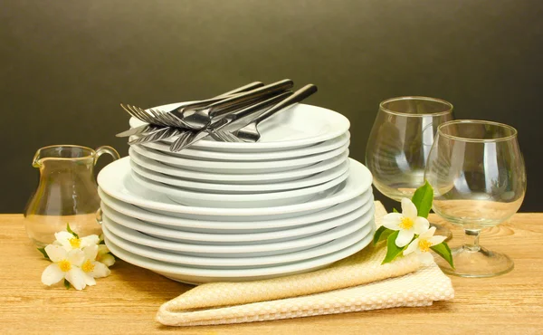 Prázdné čisté talíře a skleničky na dřevěný stůl na šedém pozadí — Stock fotografie