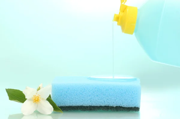 Bright sponge and flower with dish washing liquid on blue background