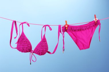 Women's swimsuit hanging on a rope on blue background clipart