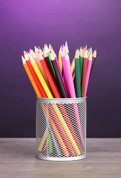 Color pencils in glass on wooden table on violet background — Stock Photo, Image