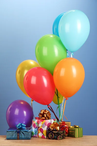 Bunte Luftballons mit Geschenken auf einem Holztisch auf blauem Hintergrund — Stockfoto