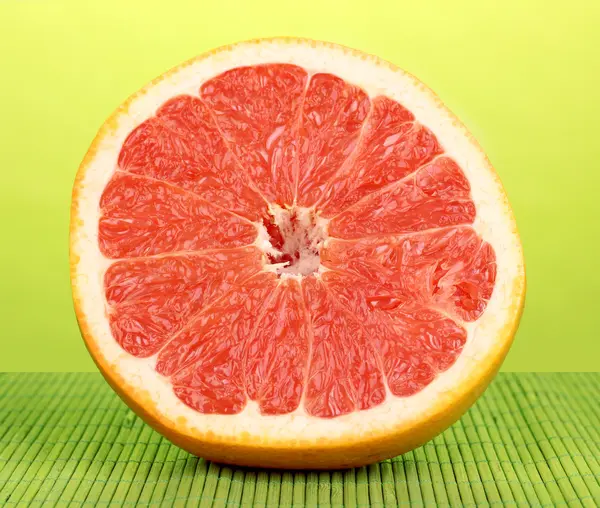 Half of ripe grapefruit on bamboo mat on green background — Stock Photo, Image
