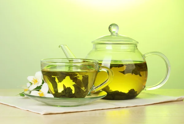 Grönt te med jasmine i kopp och tekanna på träbord på grön bakgrund — Stockfoto