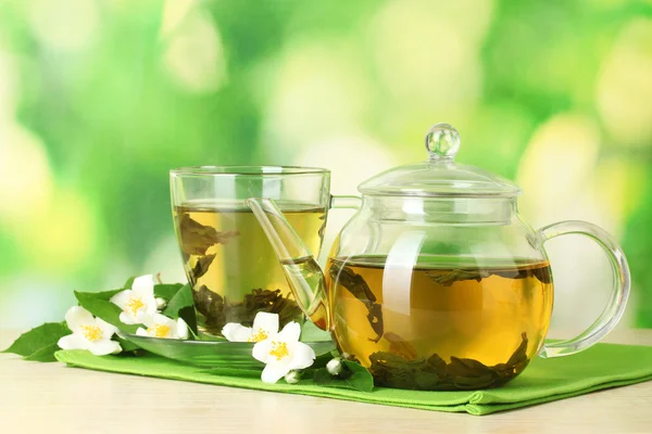 Thé vert avec jasmin en tasse et théière sur table en bois sur fond vert — Photo