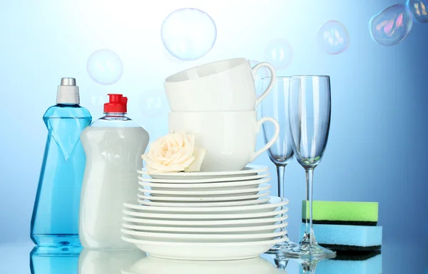 Assiettes, verres et tasses propres vides avec liquide vaisselle et éponges sur fond bleu — Photo