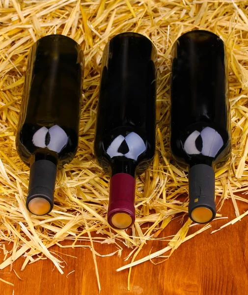 Bottiglie di grande vino su fieno su tavola di legno — Foto Stock