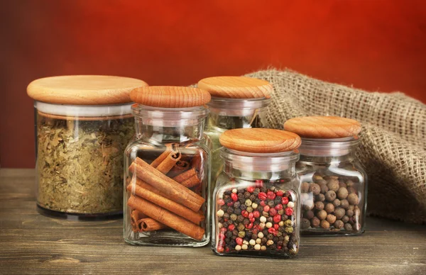 Üvegek, a fűszerek, a fából készült asztal, piros háttér — Stock Fotó