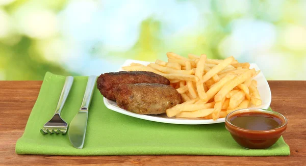 Patate fritte con hamburger sul piatto su sfondo verde primo piano — Foto Stock