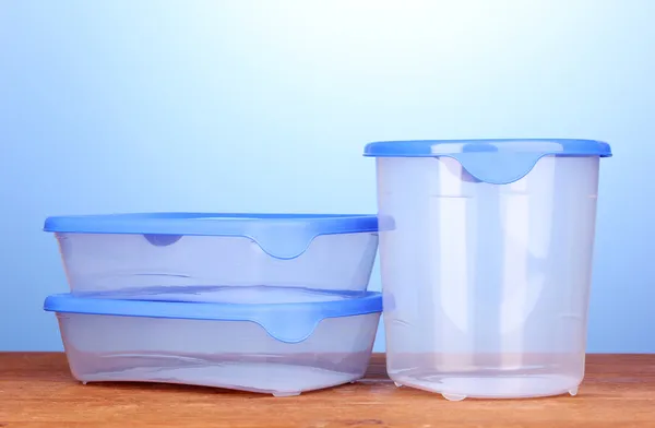 Récipients en plastique pour nourriture sur table en bois sur fond bleu — Photo