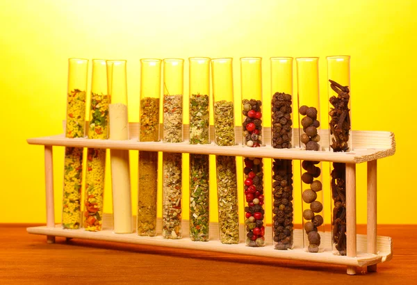 Várias especiarias em tubos na mesa de madeira no fundo amarelo — Fotografia de Stock