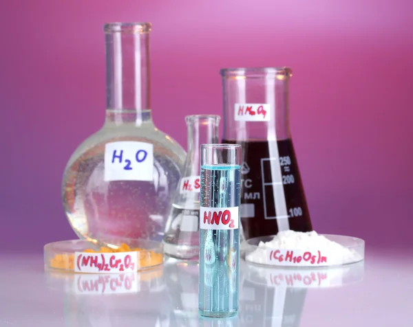 Пробирки с различными кислотами и химикатами на фиолетовом фоне — стоковое фото