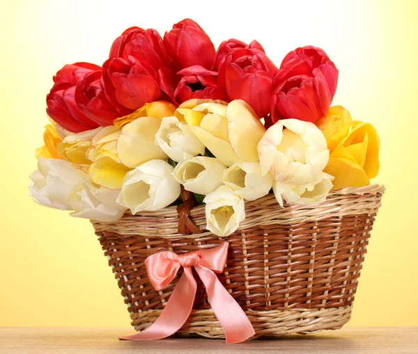 Mooie tulpen in mand op houten tafel op gele achtergrond — Stockfoto