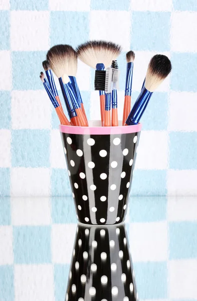 Pincéis de maquiagem em uma xícara preta de bolinhas no fundo colorido — Fotografia de Stock