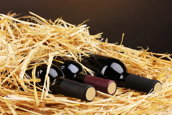 Flessen van grote wijn op hooi op bruine achtergrond — Stockfoto