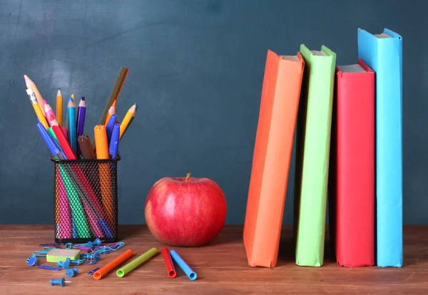 Состав книг, канцелярских принадлежностей и яблока на столе учителя на фоне доски — стоковое фото