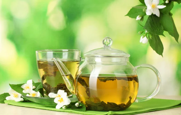 Green tea with jasmine in cup and teapot on wooden table on green background — Stock Photo, Image