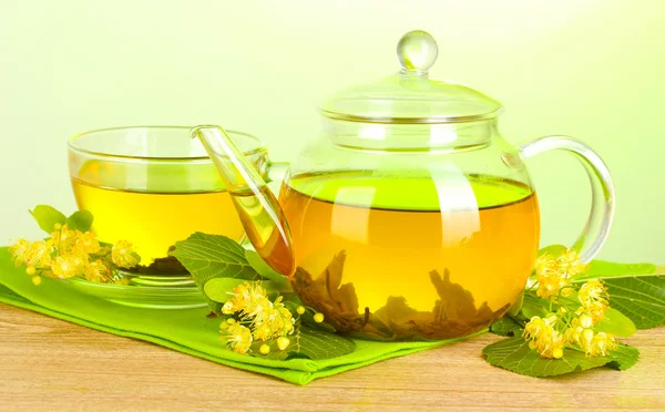 Konvice a šálek s čajem linden a květiny na dřevěný stůl na zeleném pozadí — Stock fotografie
