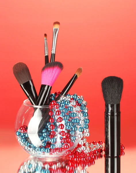 Pędzle do makijażu w misce z perłą naszyjnik na czerwonym tle — Zdjęcie stockowe