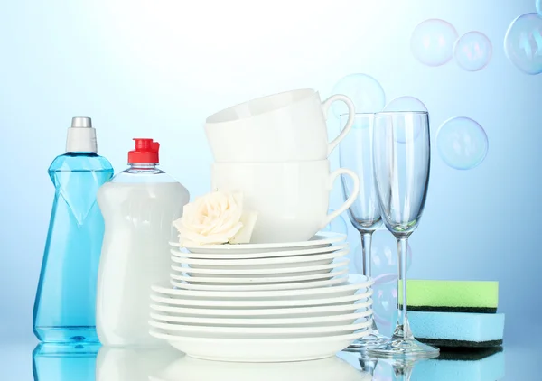 Άδειο καθαρά πιάτα, ποτήρια και κύπελλα με υγρό πιάτων και σφουγγάρια σε μπλε φόντο — Φωτογραφία Αρχείου