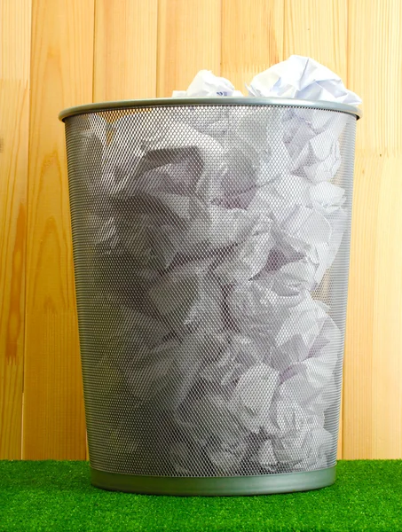 Lixo de metal bin de papel na grama no fundo de madeira — Fotografia de Stock