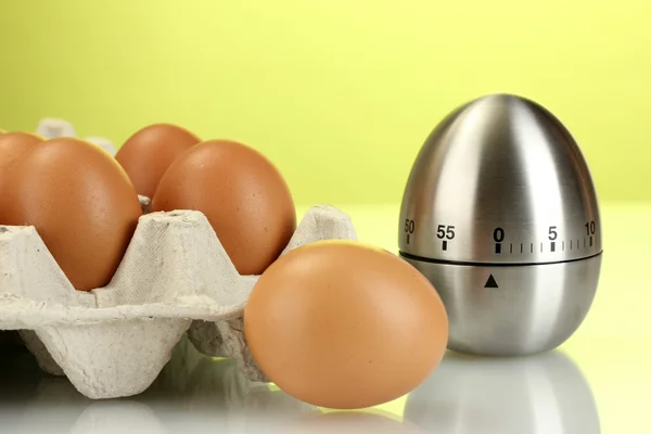 Яйца в коробке и яйцо таймер на зеленом фоне — стоковое фото