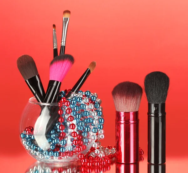 Pincéis de maquiagem em uma tigela com colar de pérolas no fundo vermelho — Fotografia de Stock