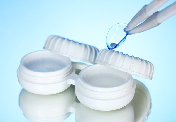Contact lenses in containers and tweezers on blue background