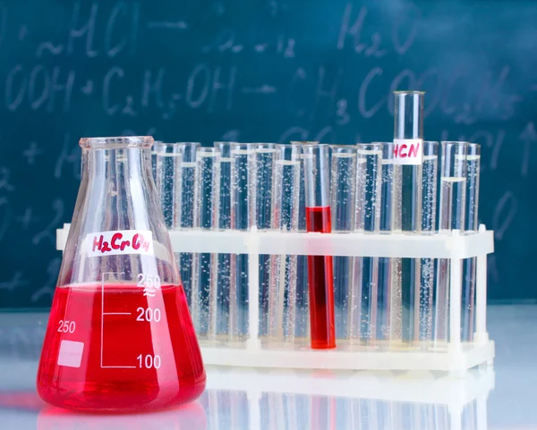 Testrør med forskjellige syrer og andre kjemikalier på bakgrunn av tavlen – stockfoto