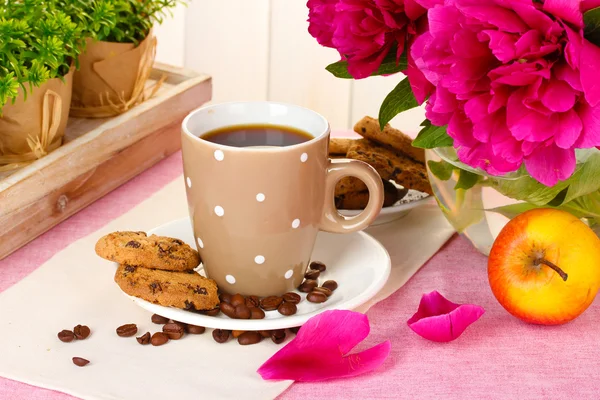 Cup of coffee, cookies, apple and flowers on table in cafe