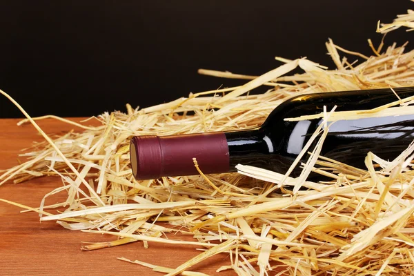 Bottiglia di grande vino su fieno su tavolo di legno su sfondo marrone — Foto Stock