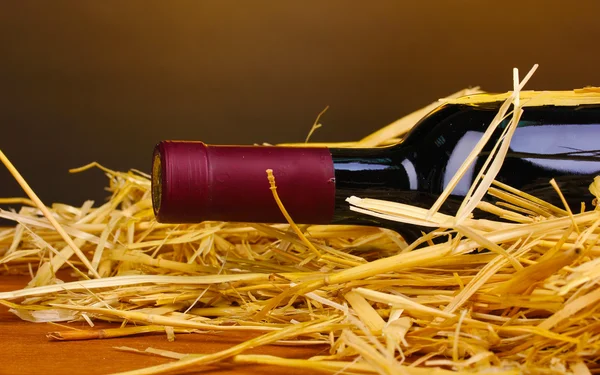 Láhev značkového vína na seno na dřevěný stůl na hnědé pozadí — Stock fotografie