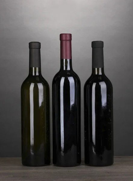 Lahví značkového vína na dřevěný stůl na šedém pozadí — Stock fotografie