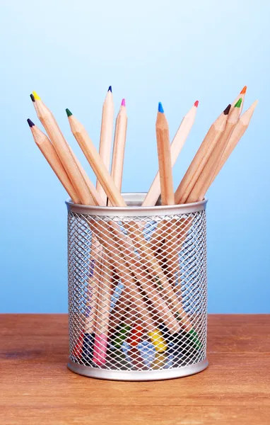 Barevné tužky ve skle na dřevěný stůl na modrém pozadí — Stock fotografie