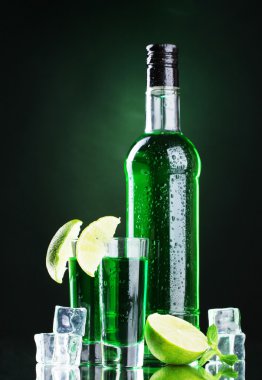 Bottle and glasses of absinthe with lime and ice on green background clipart