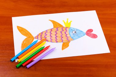 Children's drawing of golden fish and pencils on wooden background clipart