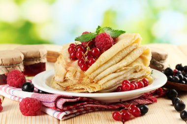 Pancakes with berries, jam and honey on wooden table on green background clipart