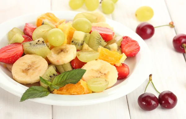 Ensalada de frutas frescas en plato y bayas en mesa de madera blanca —  Fotos de Stock