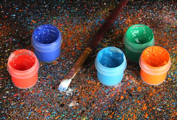 Frascos con gouache colorido y pincel sobre fondo negro, salpicado con pintura colorida de cerca — Foto de Stock