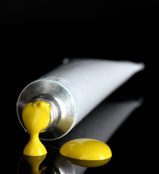 Yellow paint follows from the tube on black background close-up — Stock Photo, Image