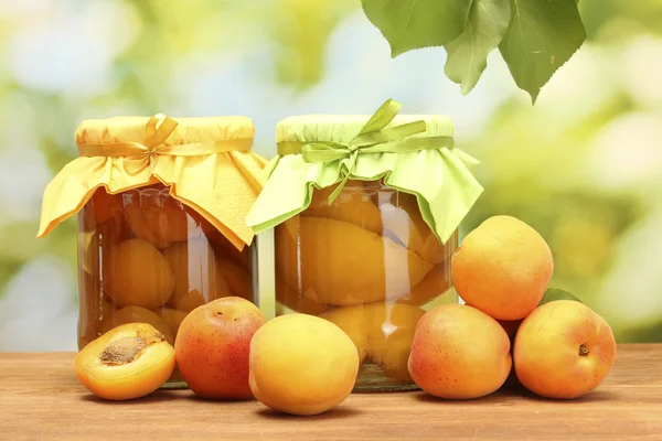 Konserverade aprikoser i en burkar och söta aprikoser på träbord på grön bakgrund — Stockfoto