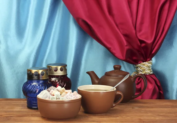 ティーポットとカップとソーサーはカーテンのクローズ アップの背景に木製のテーブルの上の甘いトルコ菓子 — ストック写真