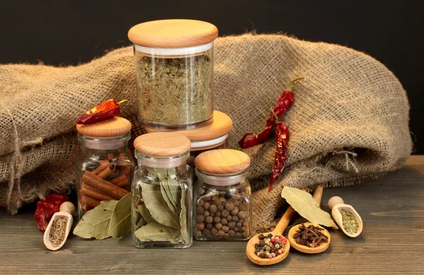 Jars and spoons with spices on wooden table on black background — Stock Photo, Image