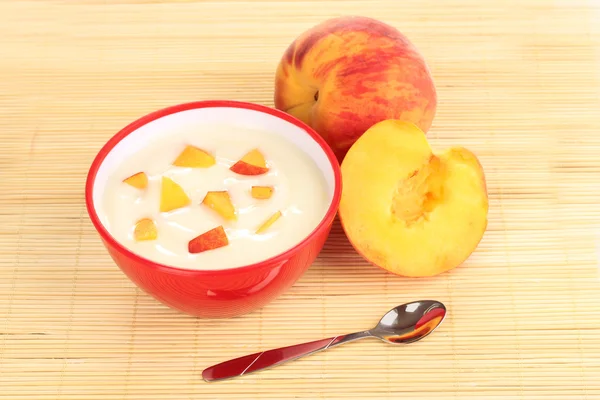 Yoghurt with peach in bowl on bamboo mat — Stock Photo, Image