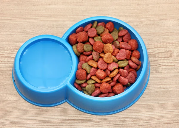 Dry dog food and water in blue bowl on wooden background — Stock Photo, Image