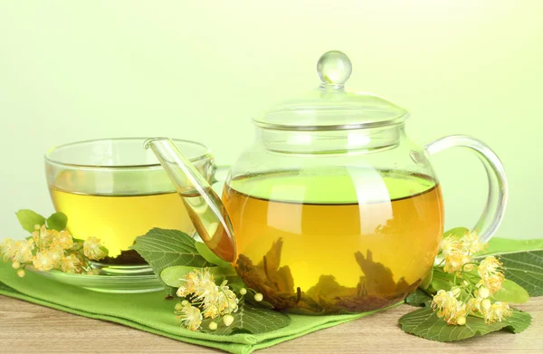 Чайник і чашка з липовим чаєм і квітами на дерев'яному столі на зеленому фоні — стокове фото