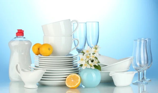 Assiettes propres vides, verres et tasses avec liquide vaisselle et citron sur fond bleu — Photo