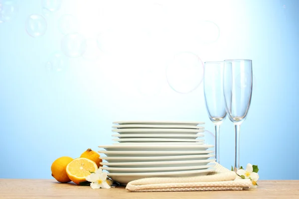 Assiettes et verres propres vides et citron sur table en bois sur fond bleu — Photo